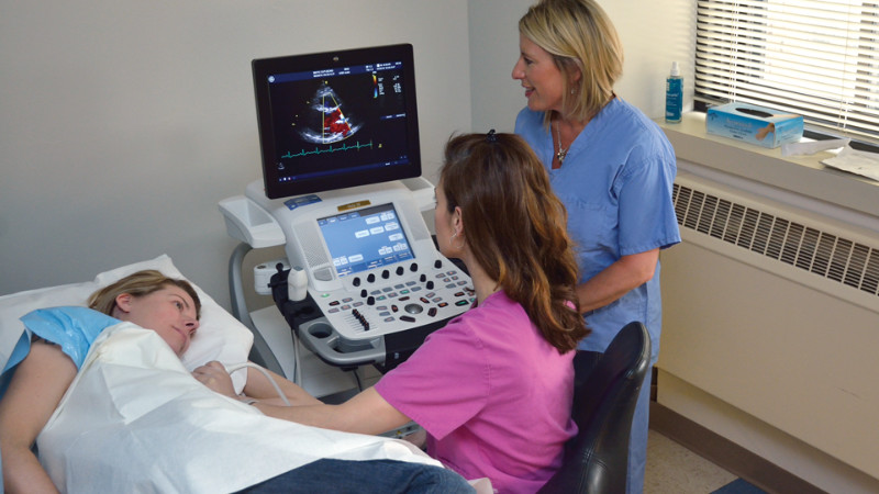 A cardiovascular technologist examining a lying patient