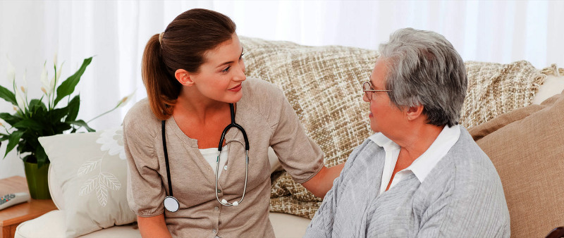 A female hospice aide sitting on a sofa with an elderly woman