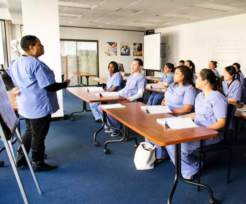a class of medical assistants sitting at desks in front of a instructor