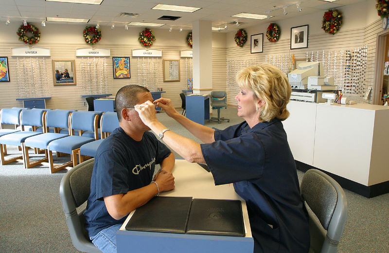 An female optician putting the glasses on client's face and adjusting the rim