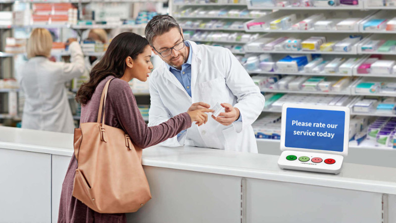 A male pharmacy technician behind a counter counseling a client in a drug store