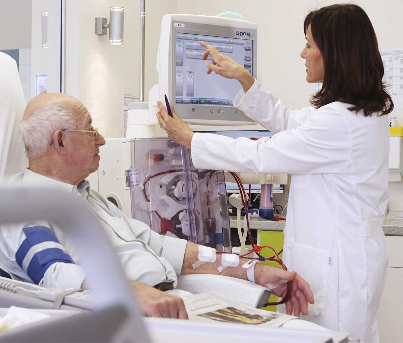 A female renal dialysis technologist operating a dialysis machine attached to an elderly patient 
