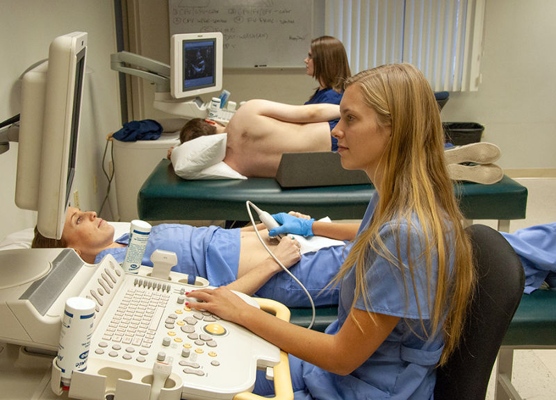 A female sonographer working at a sonograph machine and examining a patient